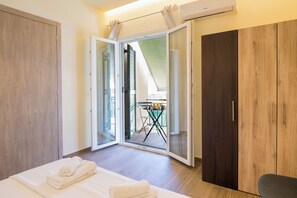 Une chambre d’hôtel comprenant un lit, une armoire et une porte-fenêtre coulissante donnant sur un espace extérieur avec une table et des chaises.