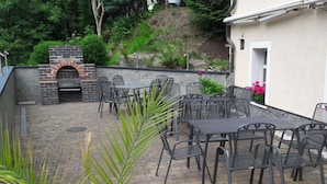 An outdoor patio with brick flooring, metal tables and chairs, and a brick oven. - Holiday Apartment Comfortable Vacation Home (Annaberg-Buchholz)