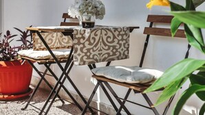 Un petit espace extérieur aménagé avec une table et deux chaises, un pot de fleurs et une fleur jaune.