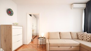 Un salon moderne avec un meuble en bois, un canapé beige et une petite table d’appoint sur laquelle se trouve une lampe.