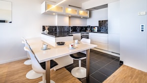 A modern kitchen with a white countertop, black backsplash, and a dining area with a white table and chairs. - Apartment by Zeedijk With Sea View (Koksijde)