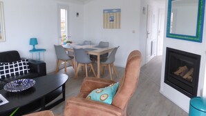 Un salon comprenant un canapé, une table basse, une table à manger avec des chaises, une cheminée et un miroir fixé au mur.