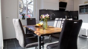 A modern kitchen with a dining area, featuring a wooden table and black chairs, a vase with flowers, and pendant lights. - House Summerlove Comfortable Vacation Home (Ostseebad Prerow)