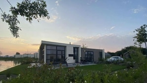 Una casa moderna de dos pisos con un amplio ventanal, un patio y un automóvil cerca.