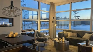 Una sala de estar moderna con ventanas amplias, una zona de comedor y un conjunto de sofás.
