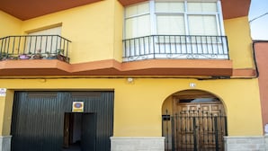 A two-story building with a yellow facade, a balcony with metal railings, and a wooden door with a metal gate.