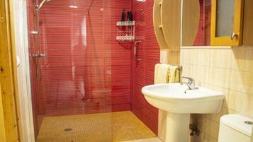 Un baño con pared de ducha en mosaico rojo, un lavamanos blanco y un inodoro.