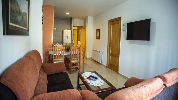 A living room with a sofa, a coffee table, and a TV mounted on the wall.