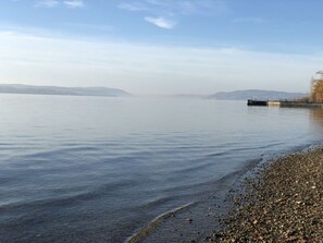 A calm lake with a pebble beach and a distant shoreline.