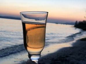 Un verre d’un liquide ambré sur une plage, avec un coucher de soleil en arrière-plan.