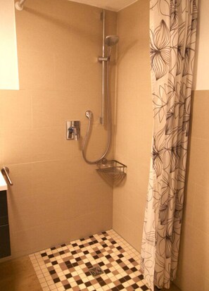 A small, tiled shower area with a showerhead, a handrail, and a shower caddy.