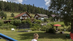 A grassy outdoor area with a slide, a trampoline, and a picnic table under a red umbrella. - Oberrain in het "vakantiehuis Schenk" (Baiersbronn)