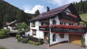 A traditional chalet-style building with a sloped roof, a balcony with red flowers, and a white facade. - Oberrain in het "vakantiehuis Schenk" (Baiersbronn)