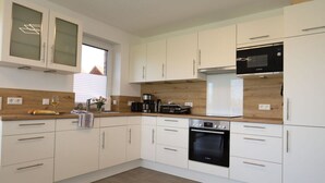 A modern kitchen with white cabinets, a black oven, a microwave, and a coffee maker. - Marinapark 147 Modern Retreat (Walchum)