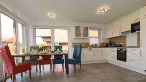 A modern kitchen with white cabinets, a dining area with red and blue chairs, and a large window providing natural light. - Marinapark 147 Modern Retreat (Walchum)