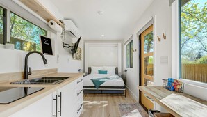 Un dormitorio compacto con cama, mesita de noche y ventana con vistas a árboles.