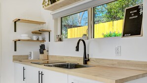 Una cocina moderna con encimera de madera, grifo negro y ventana con vista a una cerca amarilla.