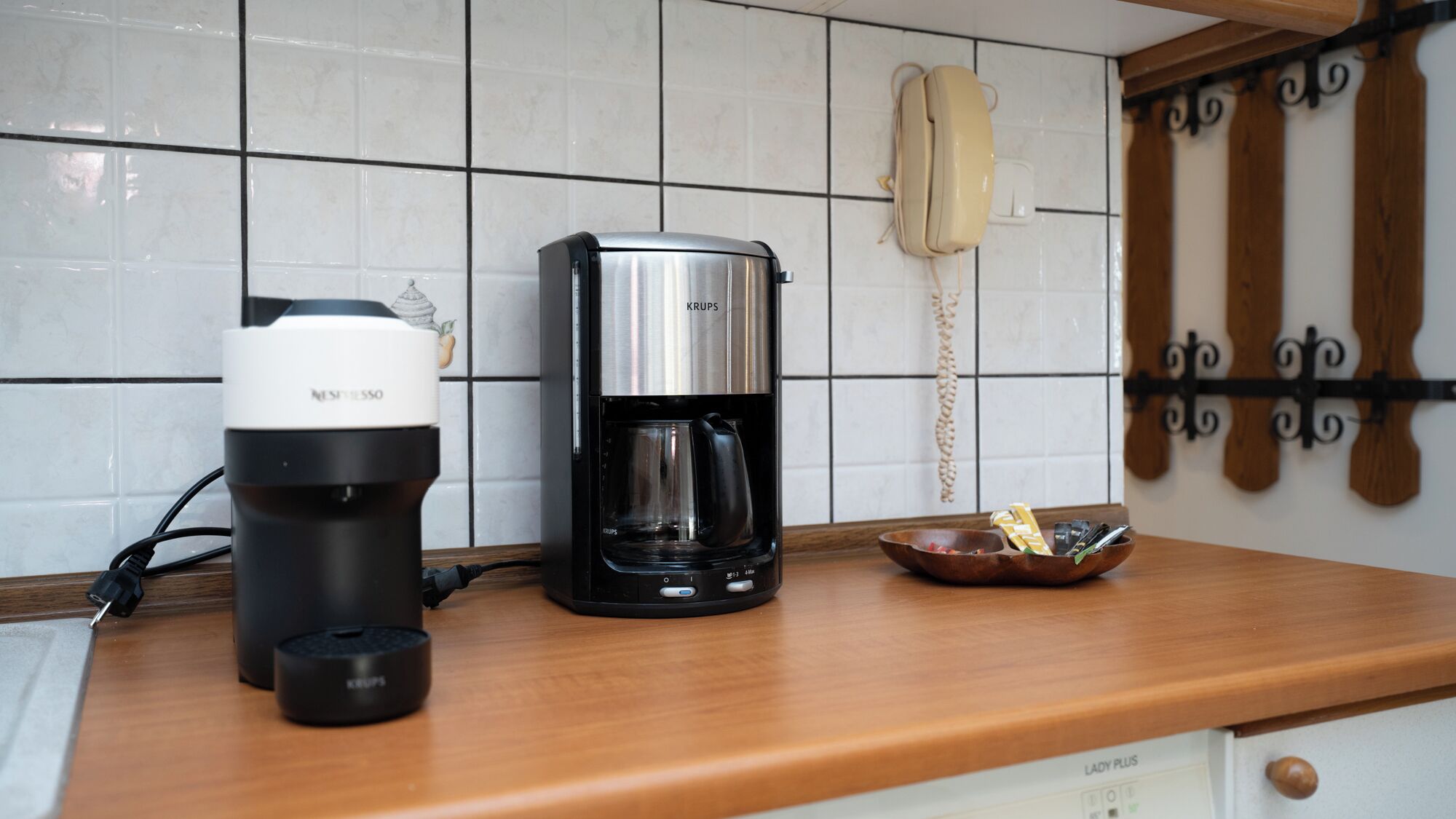 A kitchen with a coffee maker, a phone, and a bowl on the counter.
