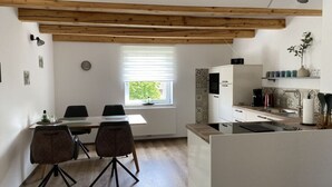 A compact kitchen with wooden beams, a dining area with two chairs, and a window with blinds. - Haus Mariechen Comfortable Holiday Residence (Frielendorf)
