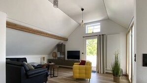 A spacious living room with a high ceiling, wooden beams, a black sofa, a yellow armchair, a TV, and a sliding glass door leading to a balcony. - Haus Mariechen Comfortable Holiday Residence (Frielendorf)