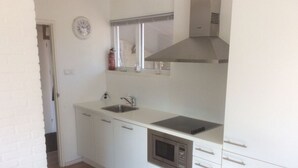 A compact kitchen with white cabinets, a stainless steel sink, a microwave, and a stove. - Holiday Home De Zilvermeeuw (Julianadorp)