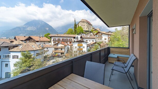A balcony with a wooden table and chairs, overlooking a town with historic buildings and a mountain in the background. - Apartment by the Stream Comfortable Holiday (Schenna)