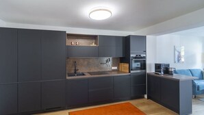 A modern kitchen with dark cabinetry, a built-in oven, and a coffee maker. - Apartment by the Stream Comfortable Holiday (Schenna)