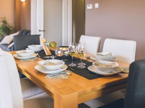Een eettafel gedekt met witte borden, kommen en wijnglazen, met een fles wijn en een klein decoratief voorwerp.
