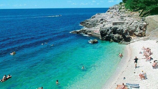 A beach with clear turquoise water, rocky cliffs, and a few people swimming and sunbathing. - Holiday Apartment DEA Vista (Medulin)