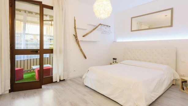 A bedroom with a large bed, a wooden door leading to an outdoor area, a wall-mounted mirror, and a hanging light fixture. - Residenza Montecatini (Montecatini Terme)