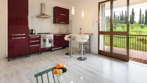A modern kitchen with red cabinets, a stove, and a sink. There's a dining area with a table and chairs, and a large window offering a view of a garden. - Residenza Montecatini (Montecatini Terme)