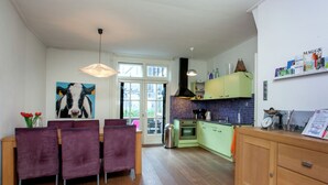 A modern kitchen with green cabinets, a wooden dining table with purple chairs, and a large painting of a cow on the wall. - Holiday Home in Alkmaar by Canal (Alkmaar)
