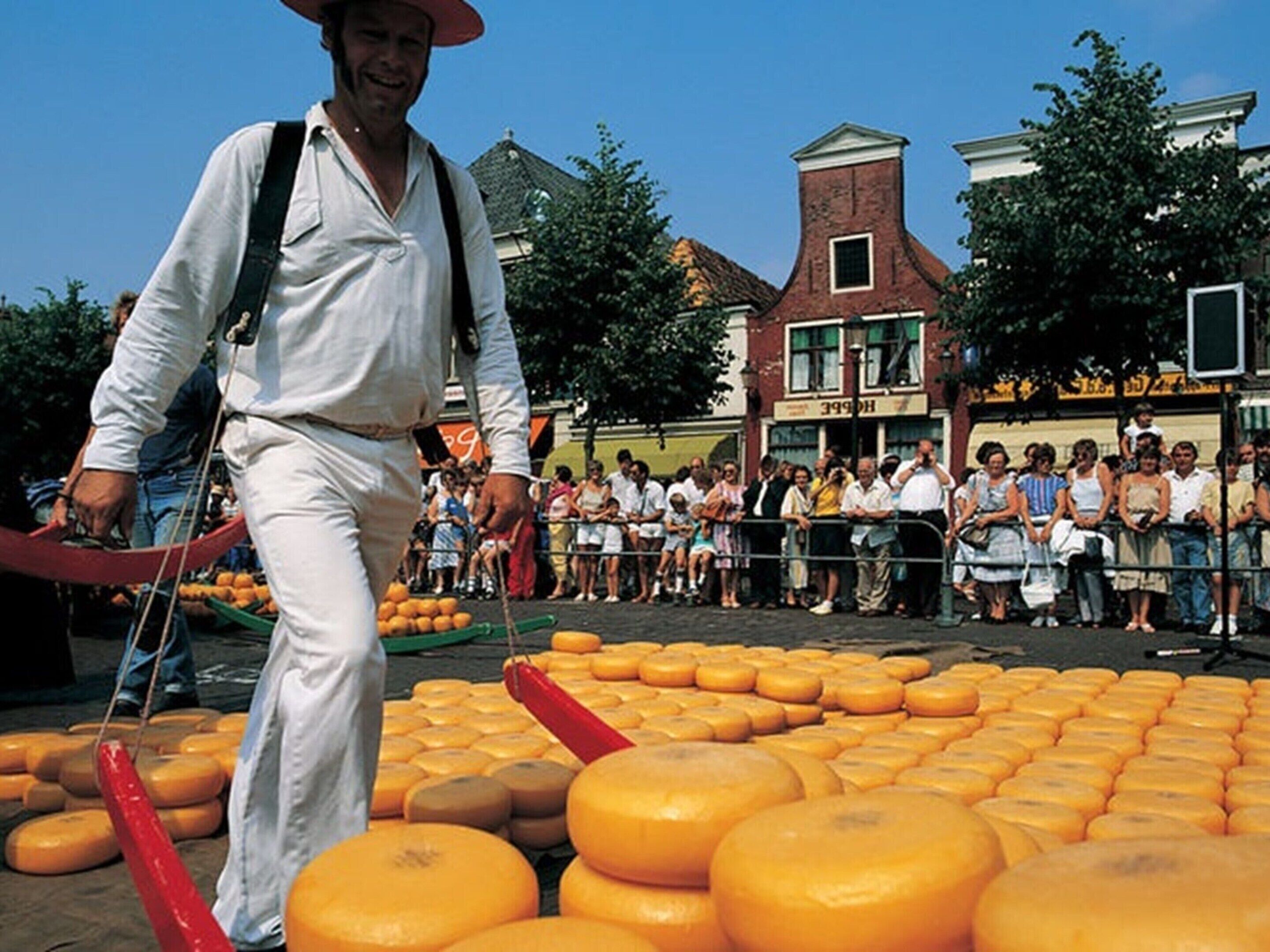 A man in white attire walking past a crowd of people, with a large display of cheese in the foreground.