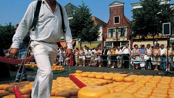 A man in white attire walking past a crowd of people, with a large display of cheese in the foreground.