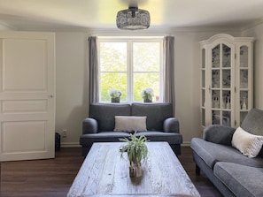 A living room with a sofa, a coffee table with a plant, a cabinet with glass doors, and a window with curtains. - 4 Star Holiday Home in Bro (Bro)