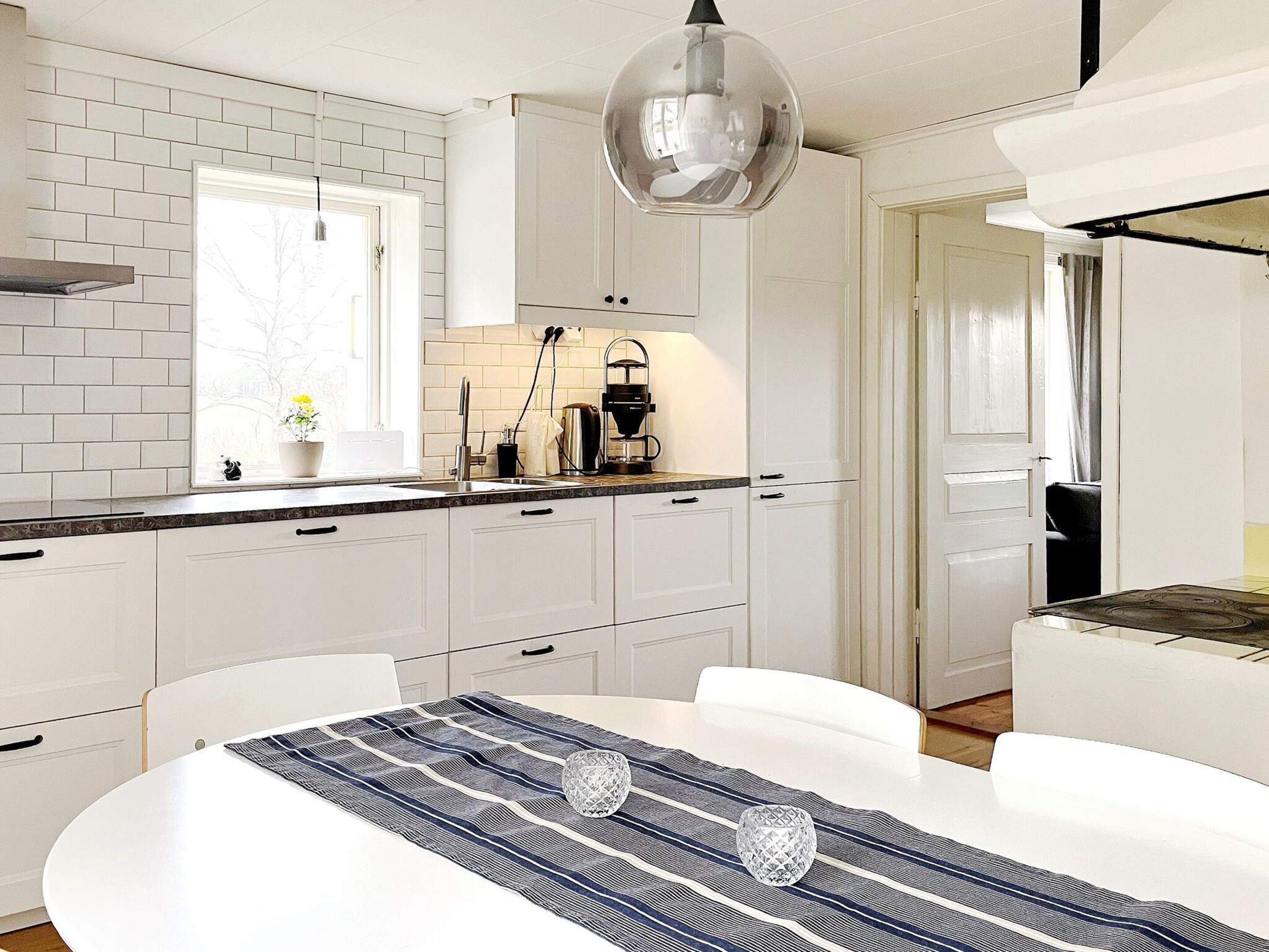 A modern kitchen with white cabinetry, a round dining table, and a hanging light fixture.