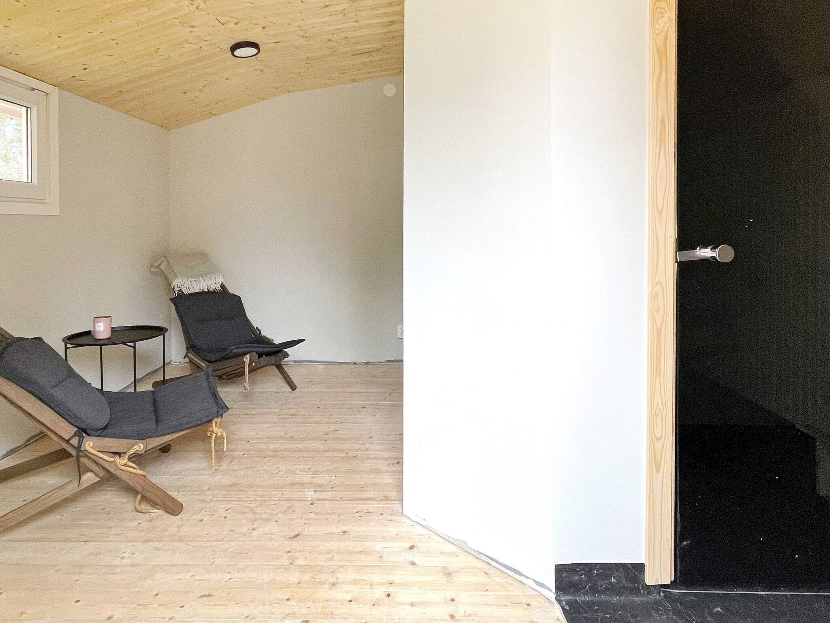 Une pièce avec un plafond haut, un plancher en bois et deux chaises noires, ainsi qu’une petite table et un objet rose posé dessus.