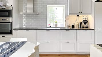 A modern kitchen with white cabinetry, a stainless steel range hood, a window with a view, and a coffee maker on the countertop.