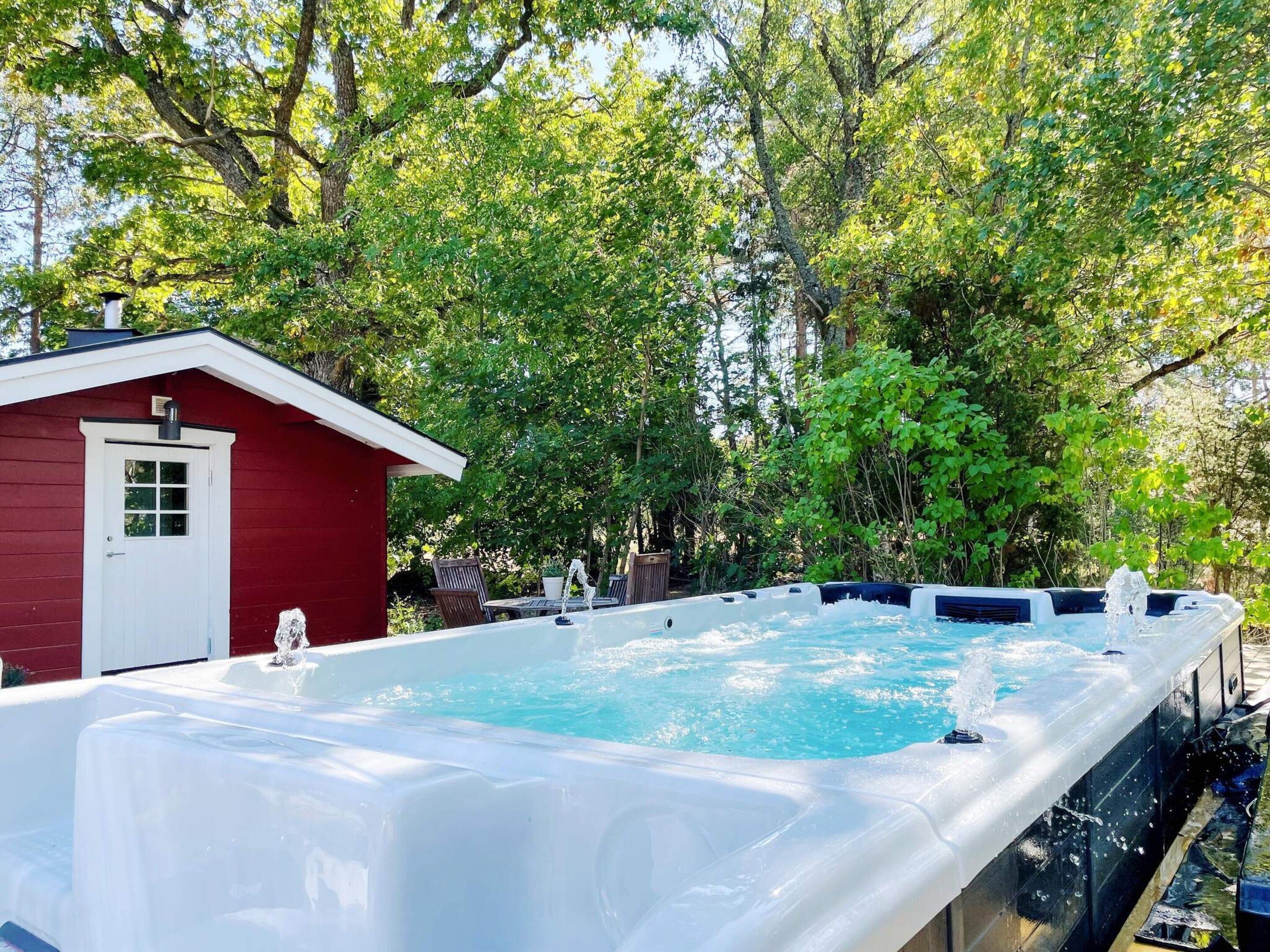 A hot tub in a backyard with a red shed and trees in the background.