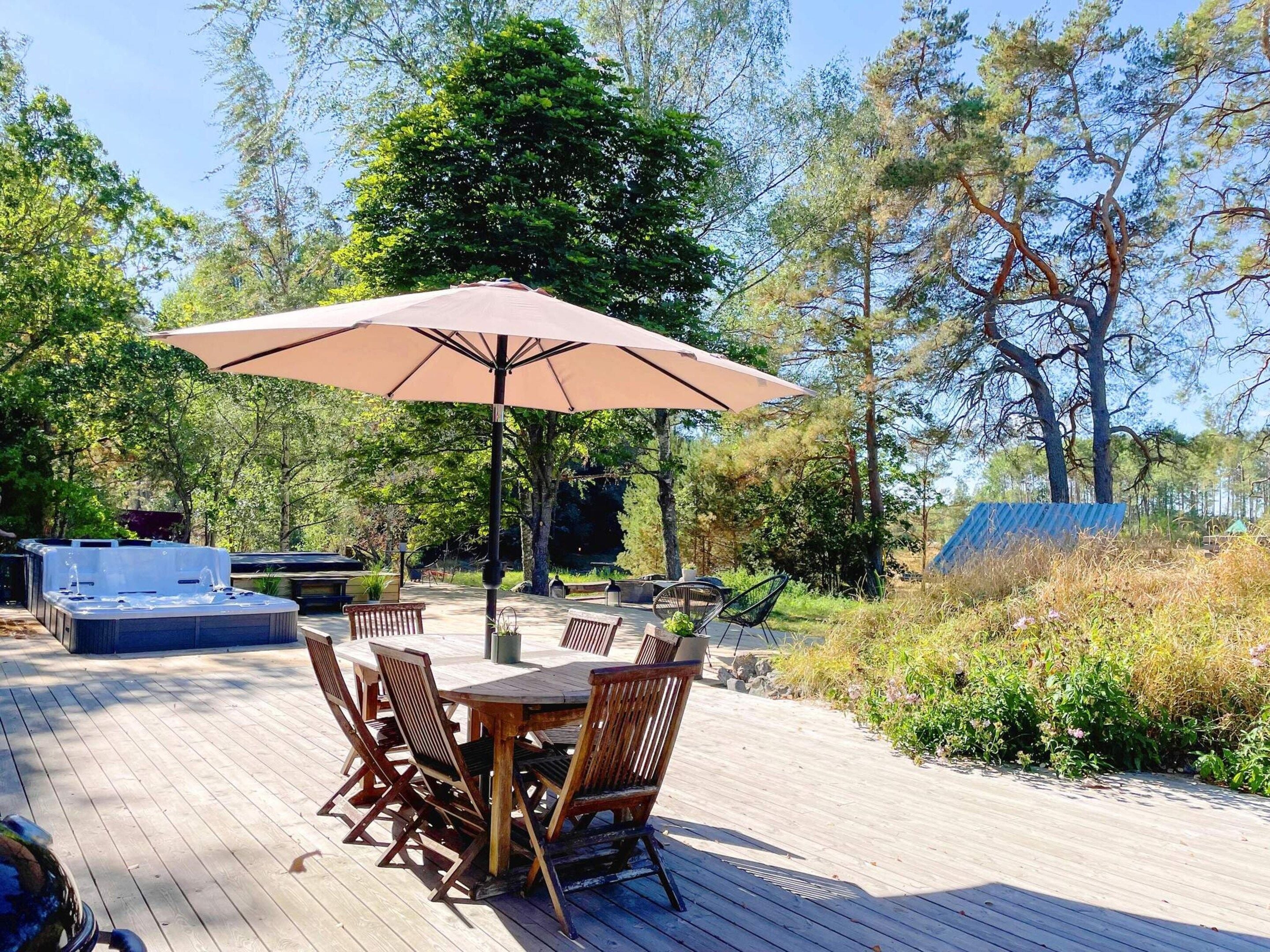 An outdoor deck with a table and chairs, surrounded by trees and a hot tub.