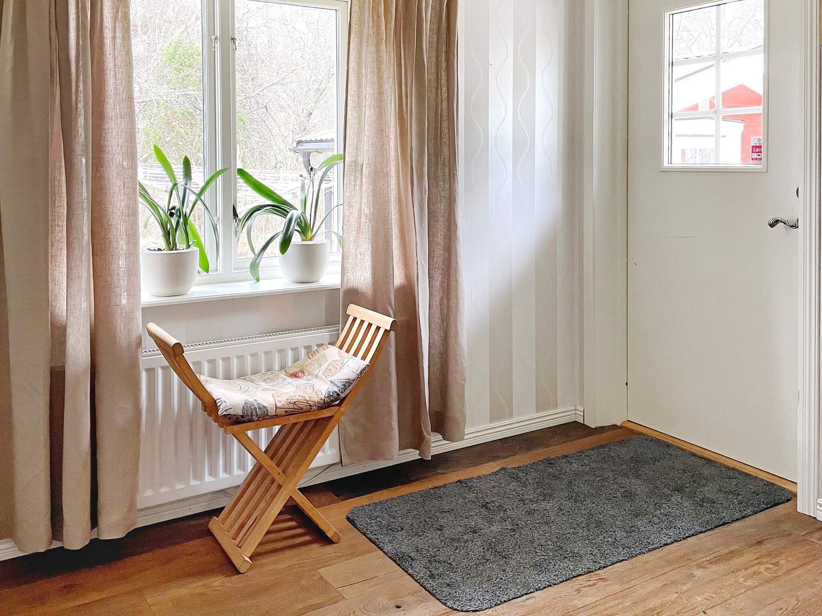 A room with a wooden chair by a window, a radiator, a grey rug, and a door with a small window.