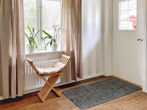 A room with a wooden chair by a window, a radiator, a grey rug, and a door with a small window. - 4 Star Holiday Home in Bro (Bro)