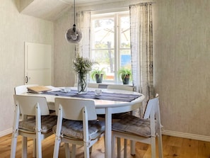A dining area with a round table, white chairs, a hanging light fixture, and potted plants. - 4 Star Holiday Home in Bro (Bro)