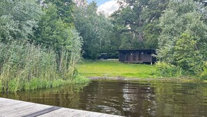 A wooden dock extending into a calm body of water, surrounded by dense greenery and a small wooden structure in the background. - 4 Star Holiday Home in Bro (Bro)