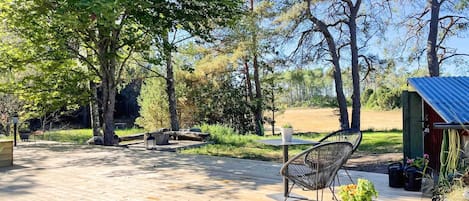 En træterrasse med udendørs møbler, et lille skur og en have med plantekasser.