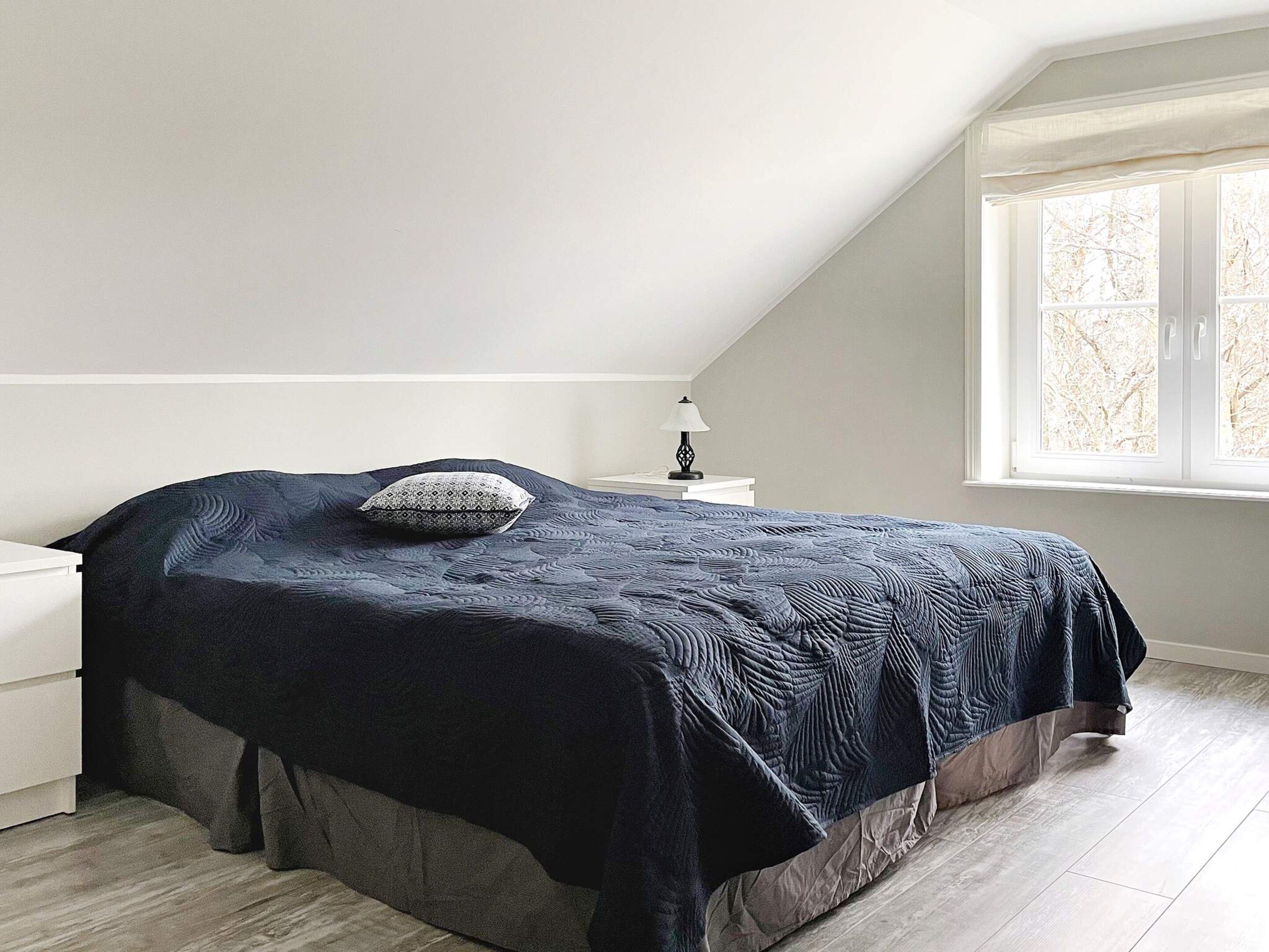 Een slaapkamer met een bed, een nachtkastje, een lamp en een raam.