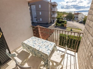 Un balcón con mesa y sillas, vista a una calle residencial y un edificio al fondo.