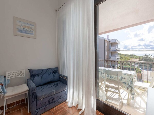 Un balcón con una mesa y sillas blancas, un sofá azul y vistas a edificios y árboles.