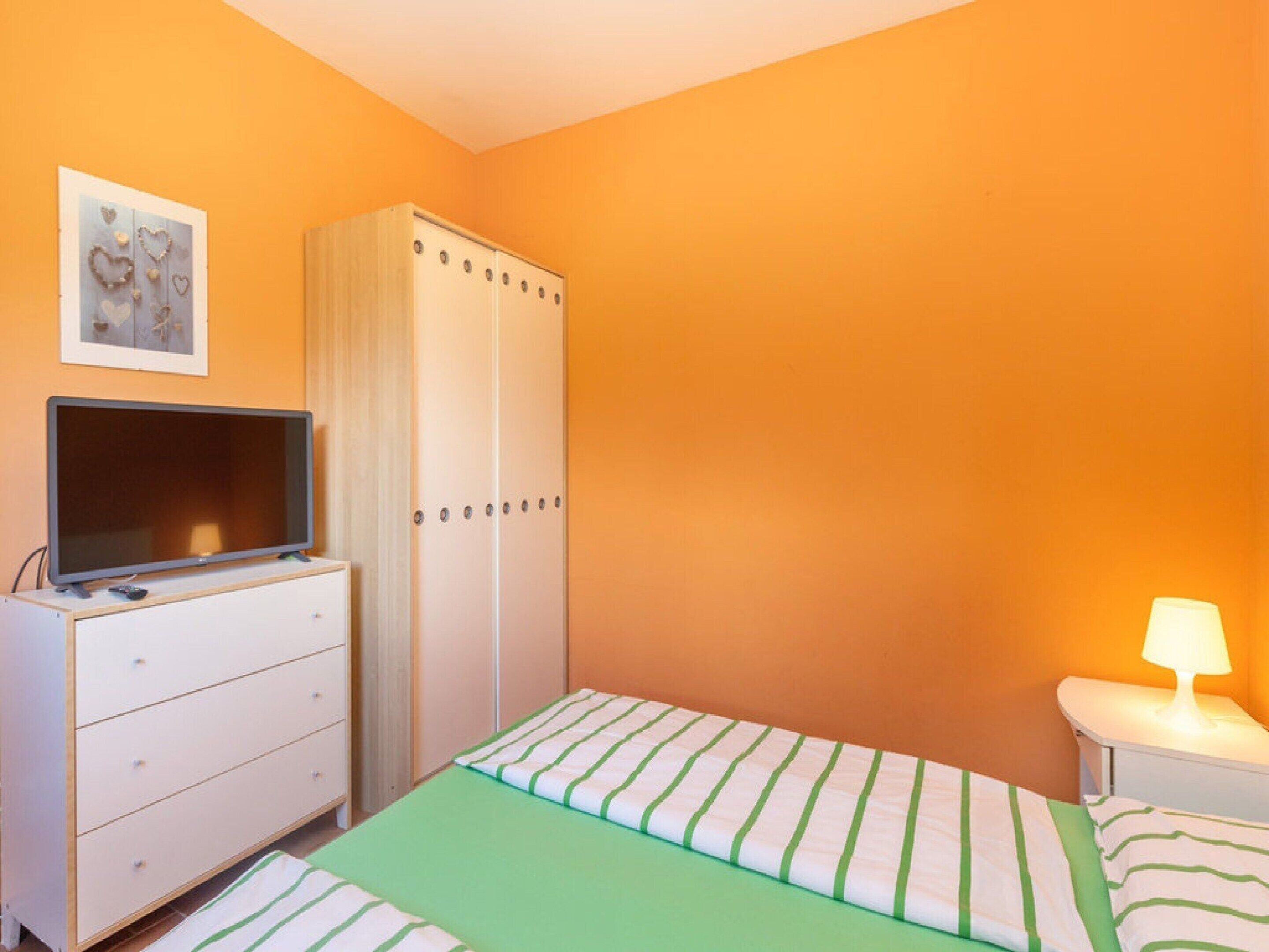 Un dormitorio con cama, cómoda, televisor, armario y lámpara de noche.