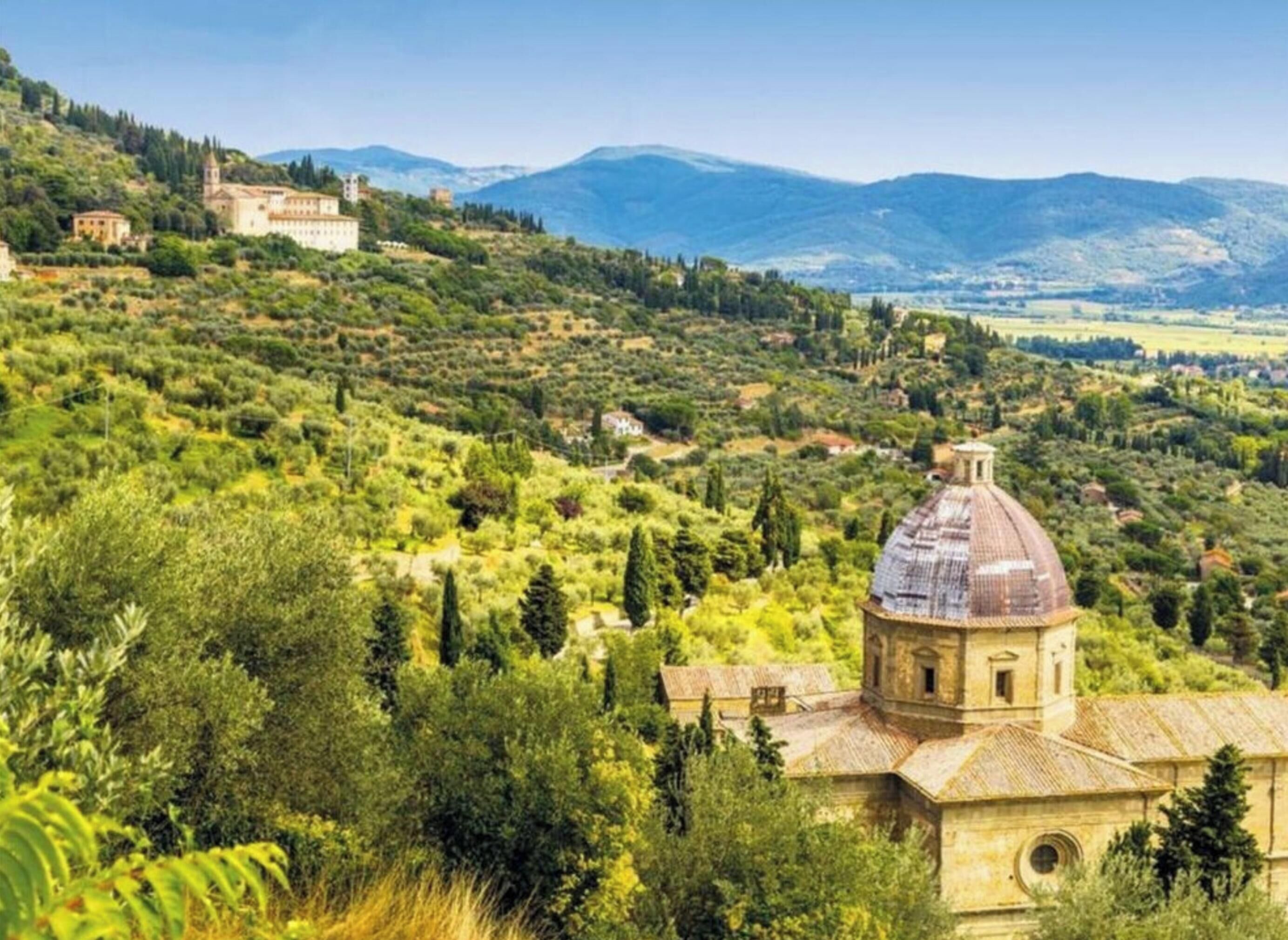 A rural landscape with a prominent church featuring a dome and bell tower, surrounded by lush greenery and hills in the background.